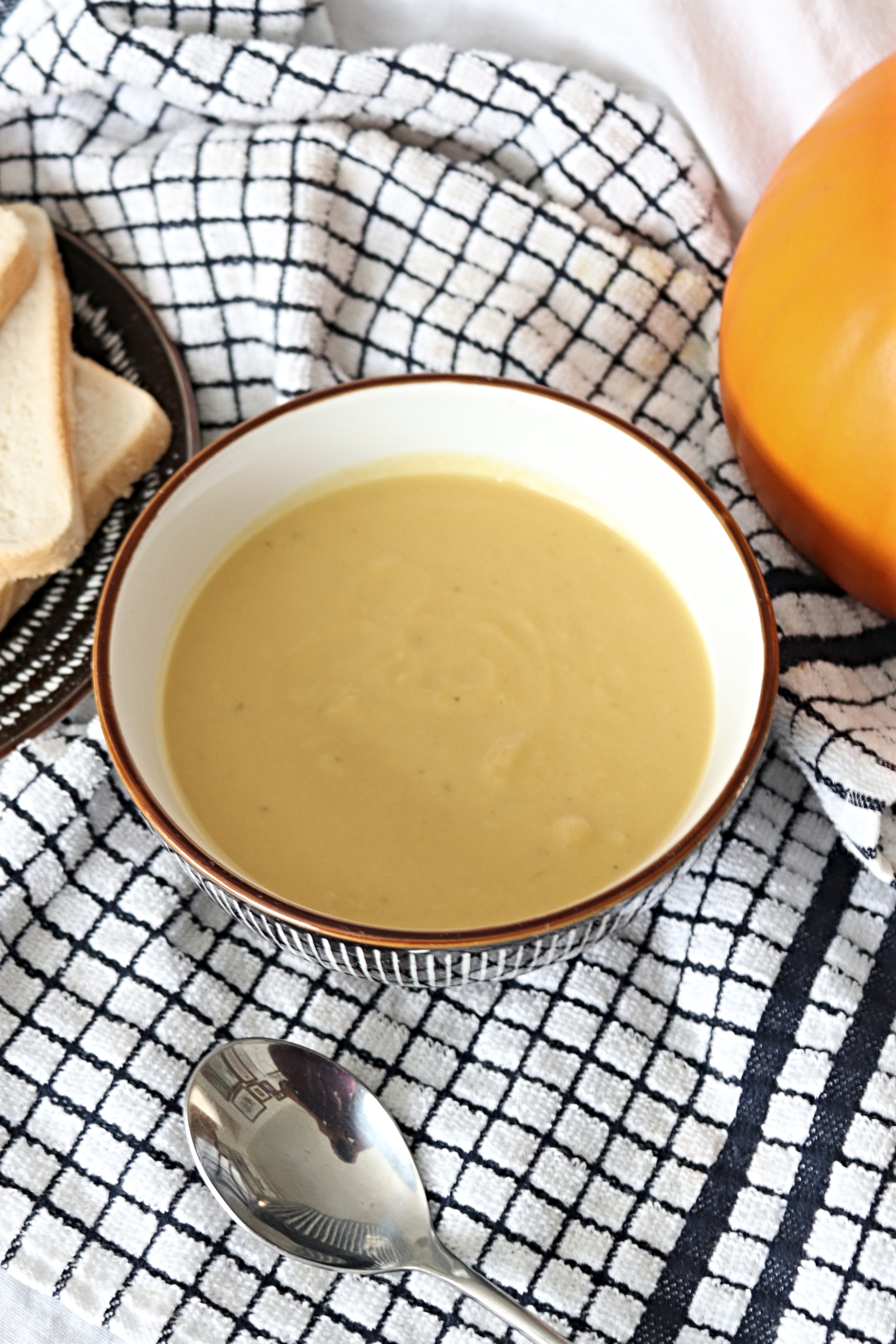 a bowl of roast pumpkin soup sat on a black and white checked tea towel