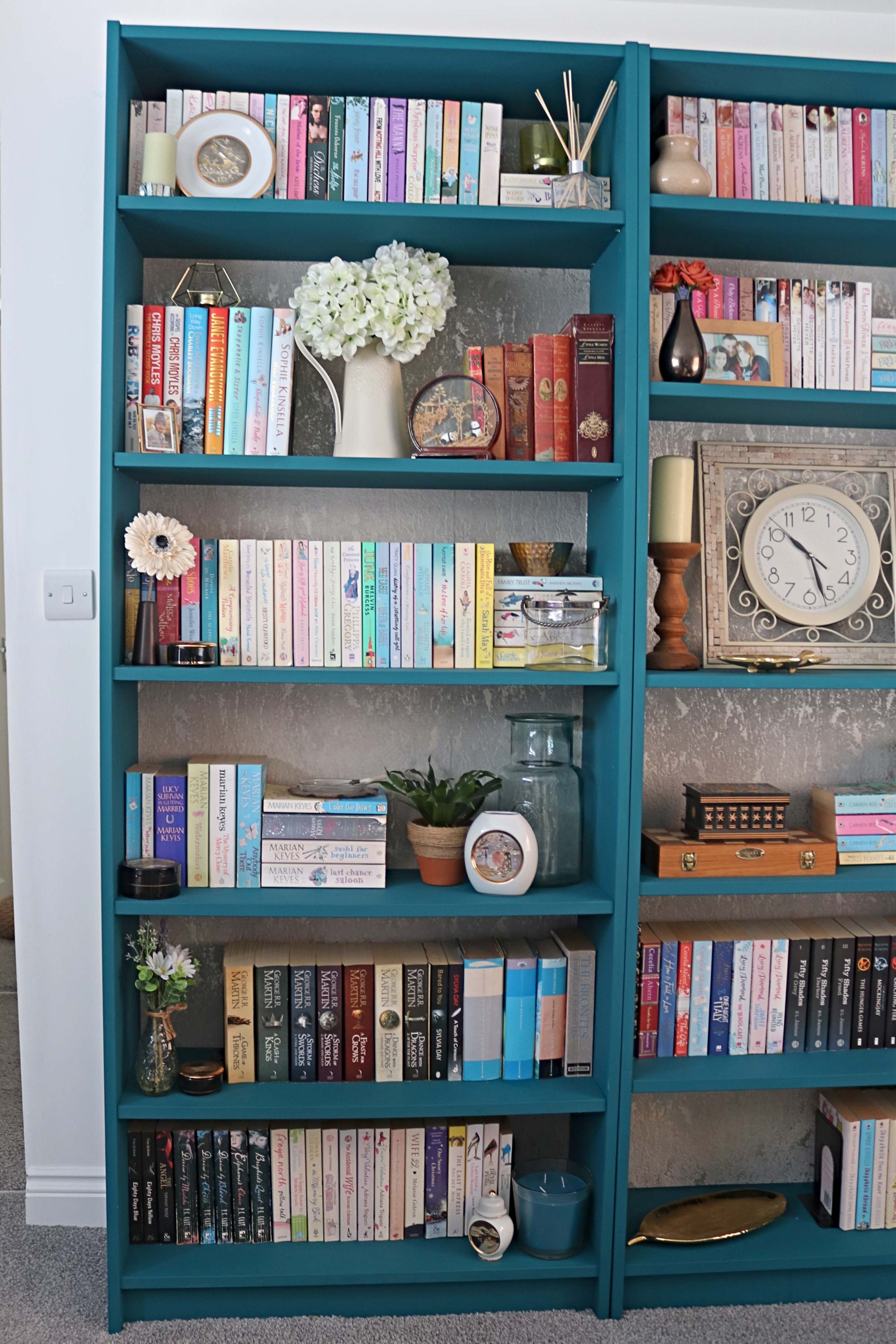 a teal green bookcase with gold flecked wallpapered back filled with books and home decor items